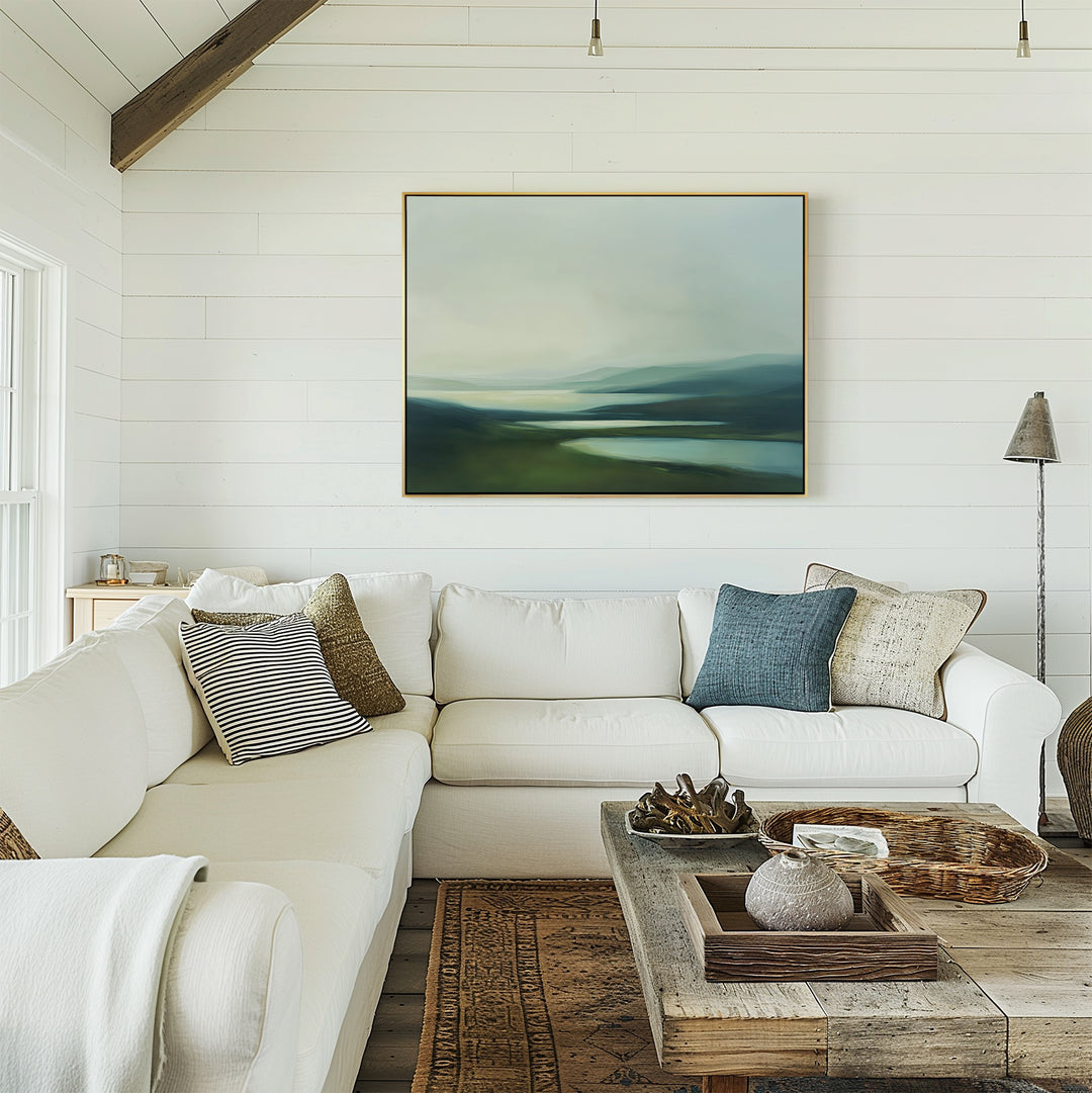 A bright, airy living room features white shiplap walls, a white sectional with pillows, a wooden coffee table with decor, and the Gentle Valleys Canvas Art – Horizontal as a serene abstract landscape above the sofa.