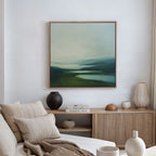 A minimalist living room showcases a beige sofa with cushions, a wooden sideboard adorned with decor, and serene wall art—a Gentle Valleys Abstract Canvas Art—framed and displayed above.