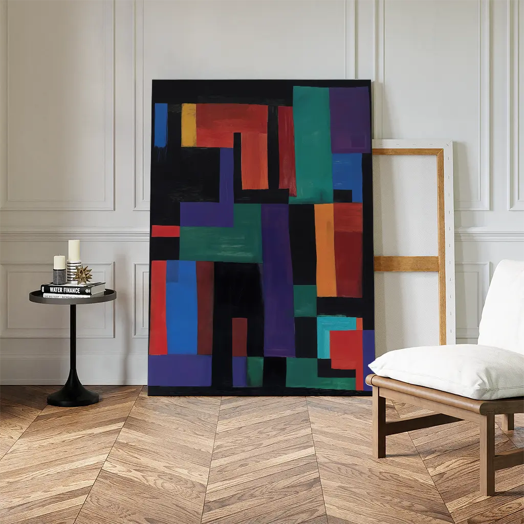 The Geometric Mosaic Canvas Art leans against a white paneled wall, bringing color and intrigue to this modern living room, alongside an empty wooden frame, black side table with candles, and a chair on a herringbone wood floor.
