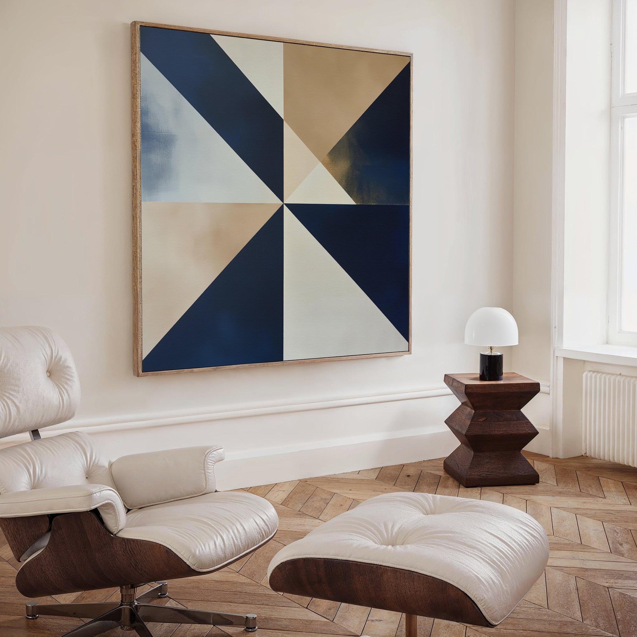 A modern living room features a cream lounge chair with ottoman, the Geometric Night Canvas Art in blue and beige, a sculptural dark wood side table, and a white table lamp by a tall window.