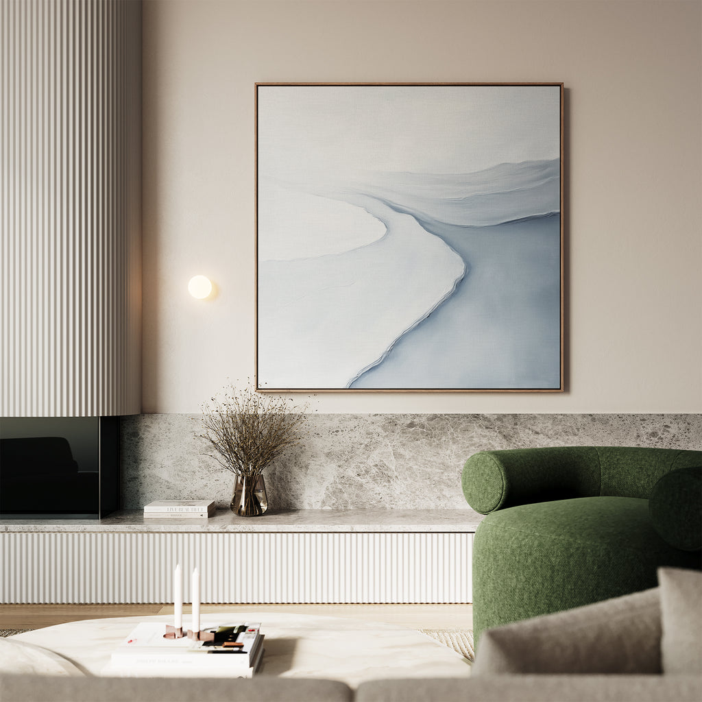A modern living room with a green curved armchair, a low marble shelf displaying decor, neutral walls, and Glacial Flow Canvas Art—a minimalist abstract canvas in soft blue and white tones.