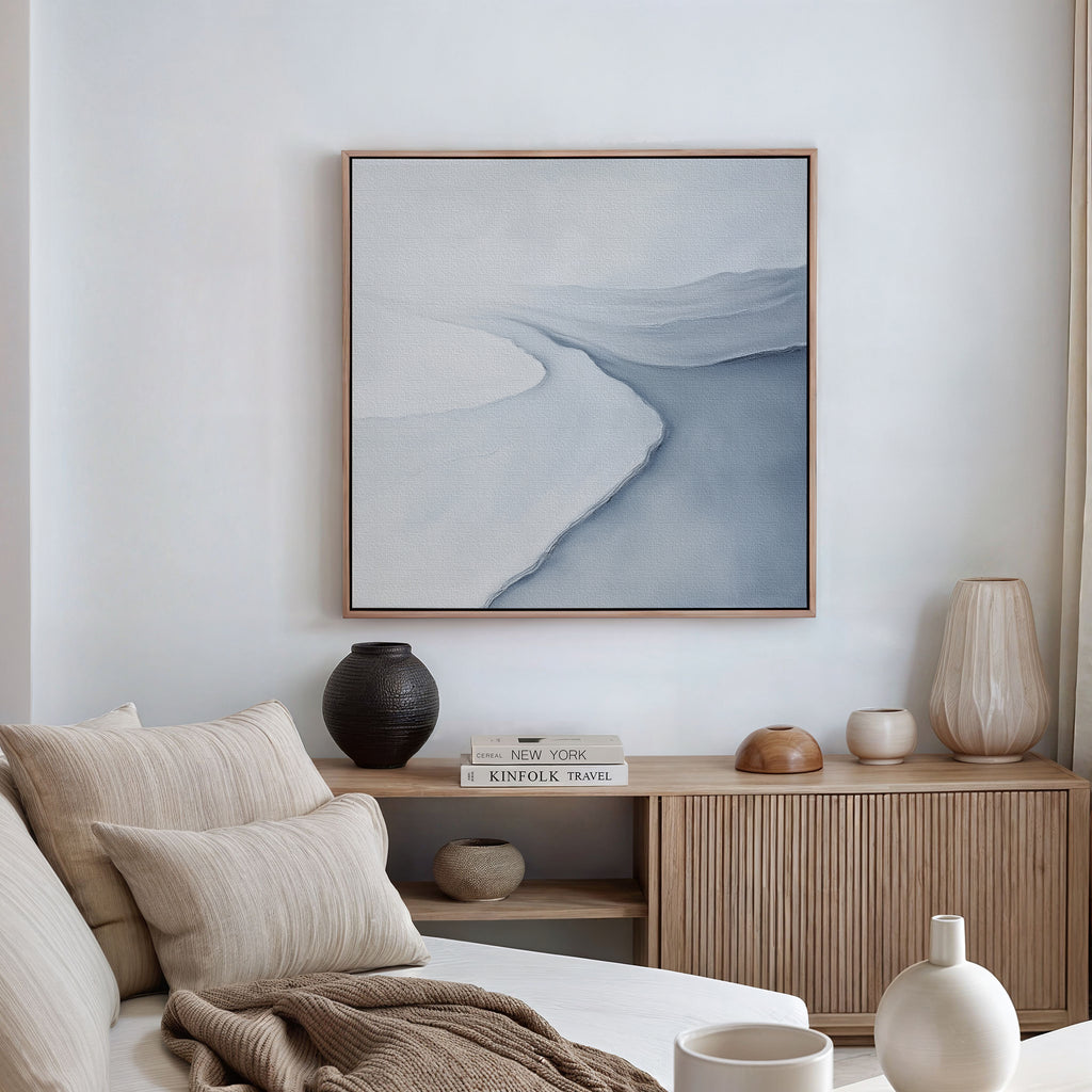 A minimalist living room with neutral tones features a cozy sofa, a wooden sideboard with vases and books, and the Glacial Flow Canvas Art in white and blue shades as striking abstract wall décor for a modern touch.