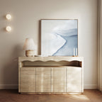 A modern console table with a wavy design displays a lamp, two tall candles, and the Glacial Flow Canvas Art in soft blue and white; two round wall lights and sheer curtains finish the modern living room decor.