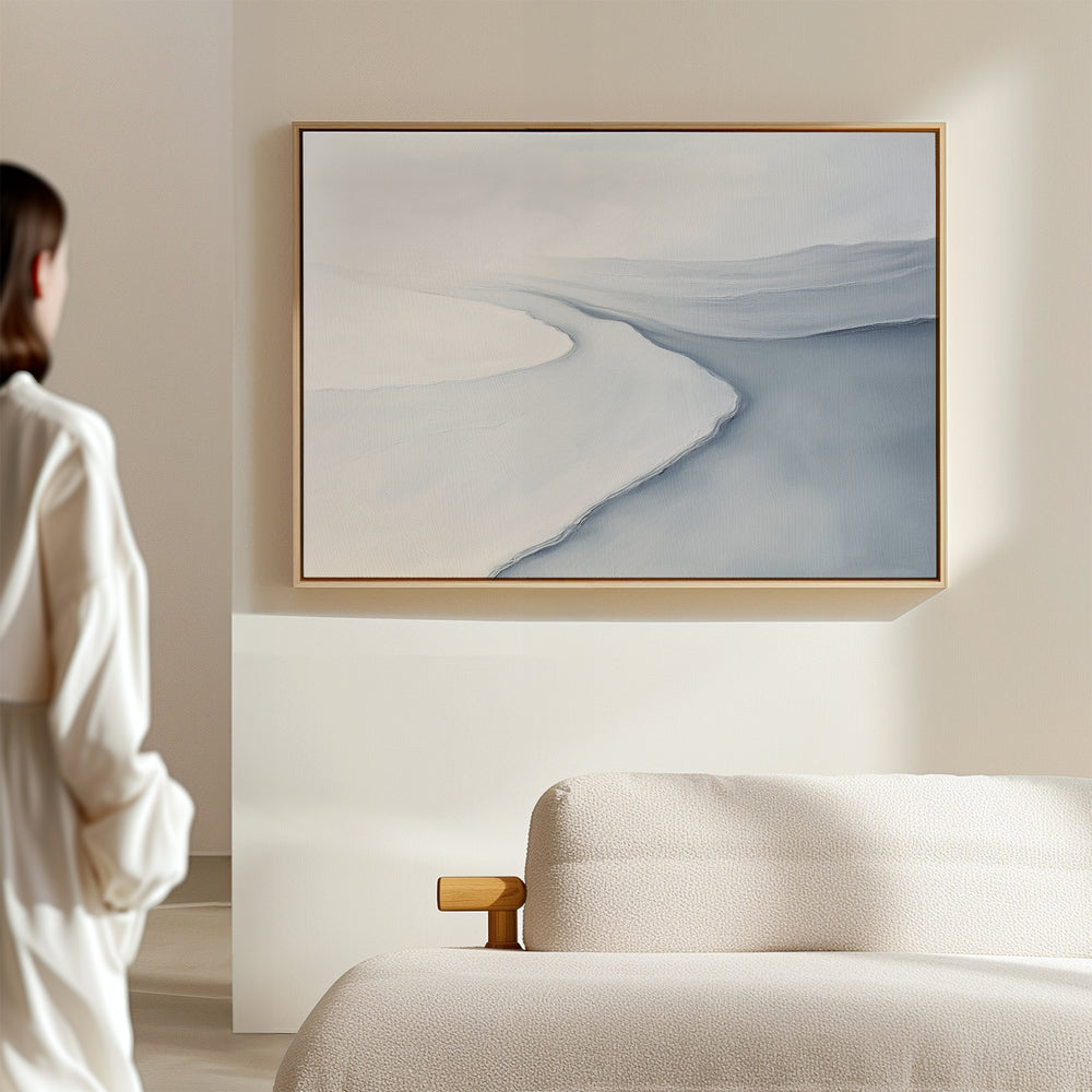 A person stands in a softly lit room, admiring the Glacial Flow Canvas Art – Horizontal with pale blue and white tones above a light-colored sofa—a perfect modern living room decor accent.