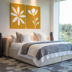 Modern bedroom with a large bed, gray and white bedding, several pillows, and the Golden Bloom Set of 2 floral wall art above the headboard. Natural light enters from a large window; two dark vases are beside the bed.