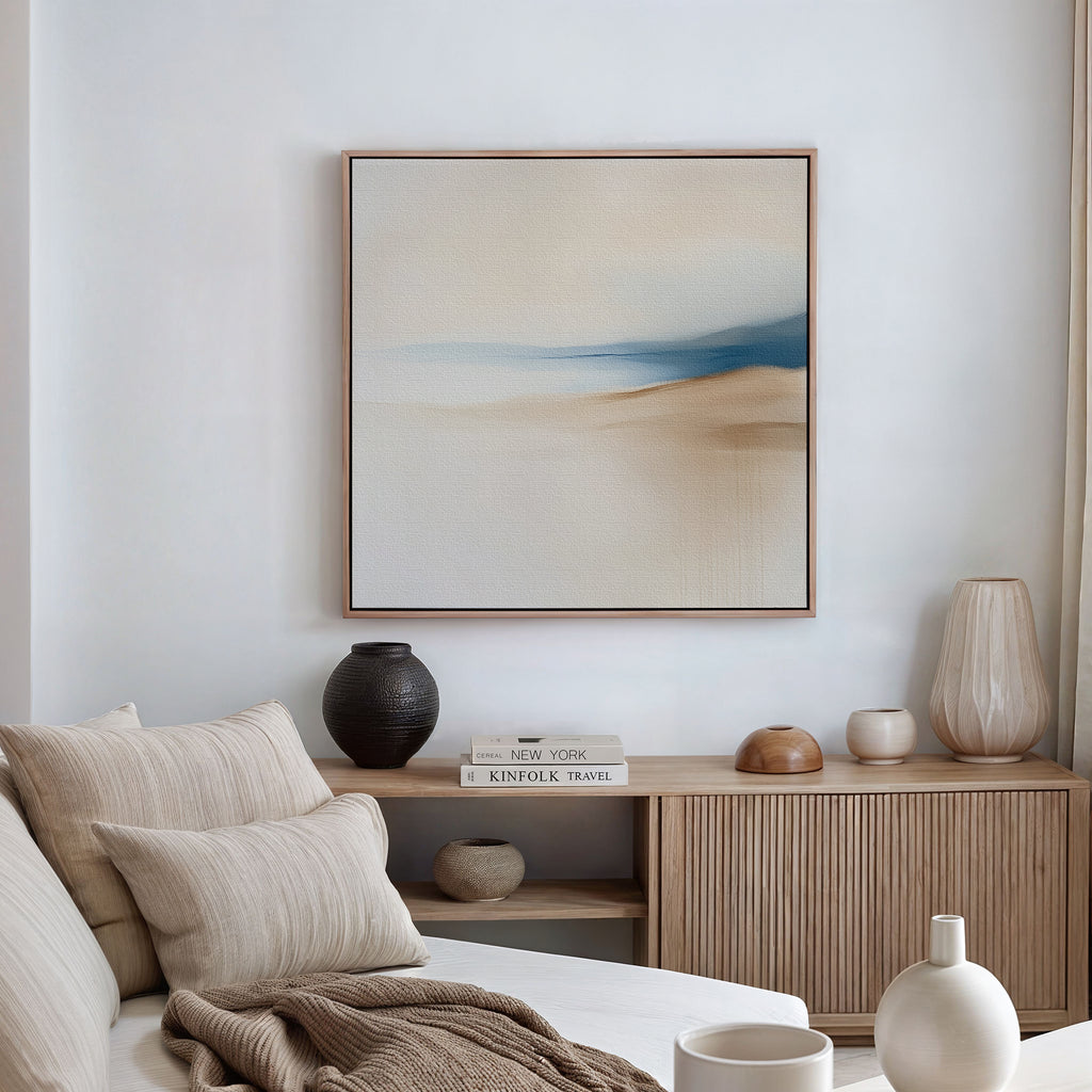 A minimalist living room featuring a cream sofa, neutral pillows, a wooden sideboard with books and vases, and the Golden Drift Canvas Art in calming beige and blue tones—perfect modern decor inspiration.