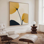 A modern living room with a white leather lounge chair and ottoman, a geometric wooden side table with a lamp, and Golden Leaves Canvas Art featuring bold yellow and black shapes. Sunlight from a tall window enhances the stylish decor.