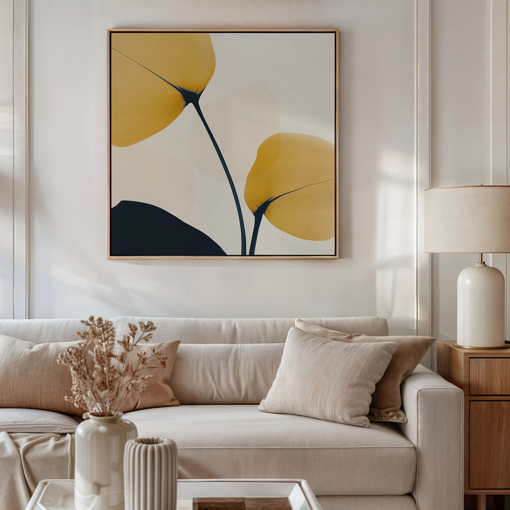 A modern living room features a beige sofa with light cushions, a side table with a white lamp, and the Golden Leaves Canvas Art in yellow and black above the sofa. A vase of dried flowers decorates the coffee table.