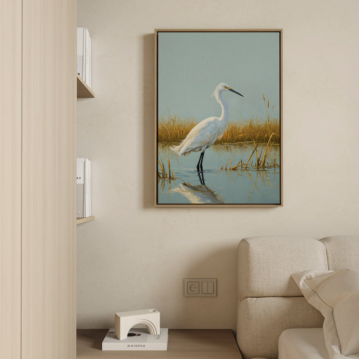 The Golden Marsh Egret Canvas Art, featuring a white egret in shallow water and tall grass, hangs above a light sofa on a beige wall, bringing serene, modern Nordic Park-inspired decor to this minimalist living room.