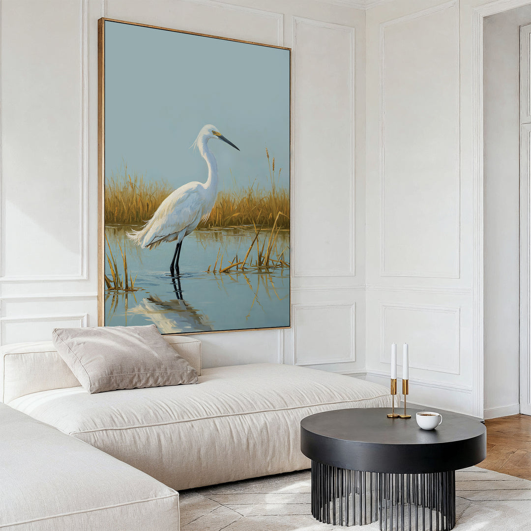 A modern living room featuring a light beige sectional, neutral pillows, a round black coffee table, and the Golden Marsh Egret Canvas Art—a serene depiction of an egret in water with reeds—brings elegant tranquility to your home decor.