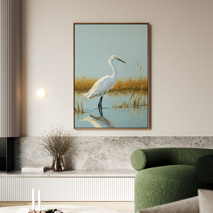 A living room with a green curved sofa, marble accents, and the Golden Marsh Egret Canvas Art—a framed painting of a white heron among golden reeds—hangs above a minimalist shelf, creating serene home decor.