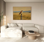 A modern living room featuring a light beige sectional sofa, round wooden coffee table, potted plant, and the Golden Plains Canvas Art showcasing a bird perched on a fence post in a golden field as nature-inspired wall decor.