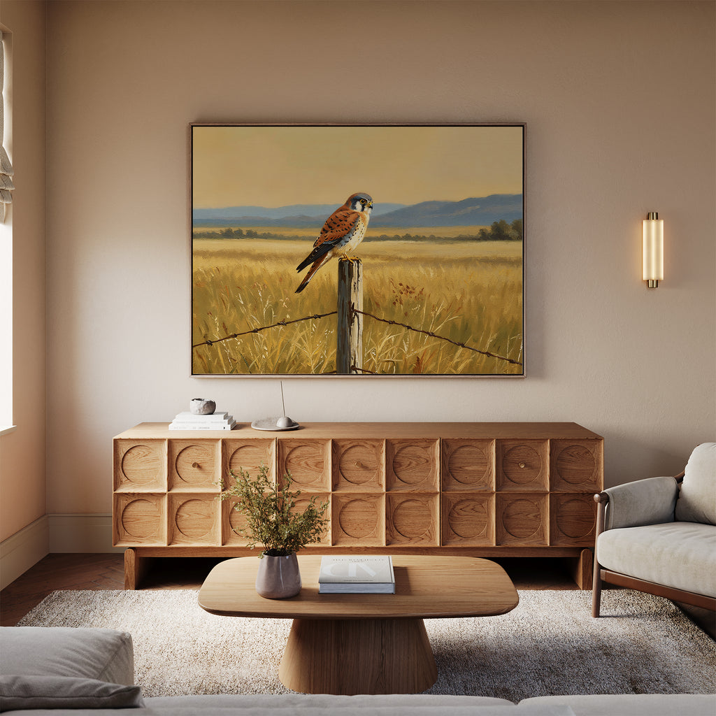 A cozy living room with a light sofa, wooden coffee table, and cabinet. Above the cabinet hangs Golden Plains Canvas Art—a large painting of a bird on a fence in a grassy field with mountains in the background.