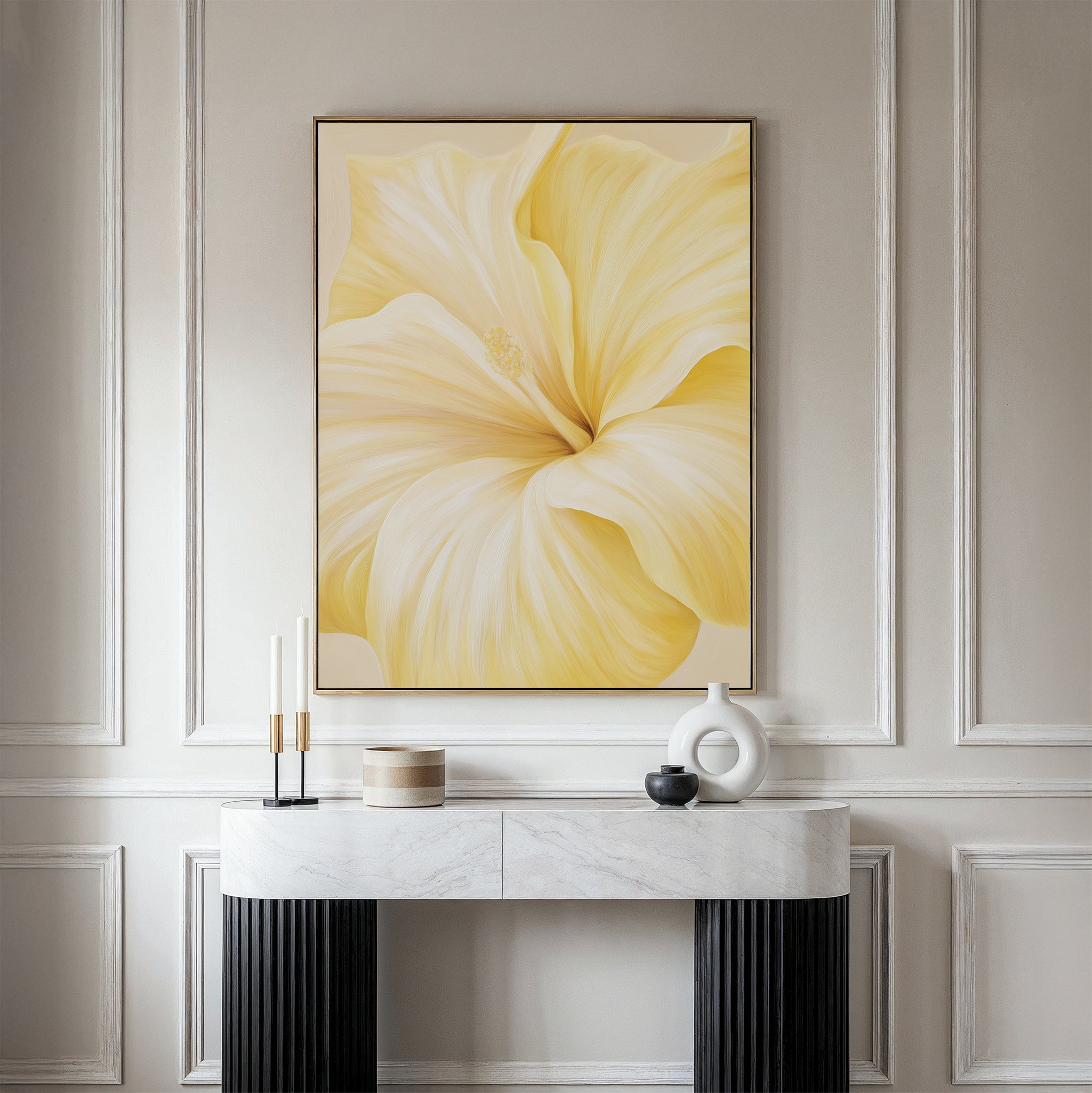 The Golden Radiance Canvas Art, a large minimalist piece with a soft yellow flower, hangs on a light gray paneled wall above a marble console table styled with candles, a round white vase, and a black bowl.