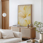A modern living room with a light wood cabinet, the Golden Radiance Canvas Art featuring yellow flowers, neutral decor, a white sofa, stacked books, ceramic vases, and a small potted plant against crisp white walls.
