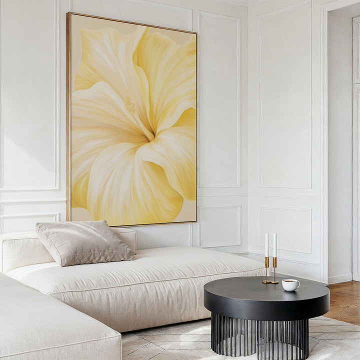 A modern living room featuring the Golden Radiance Canvas Art of a vibrant yellow flower behind a cream sectional sofa, with a round black coffee table holding candles and a cup, set against elegant white paneled walls.