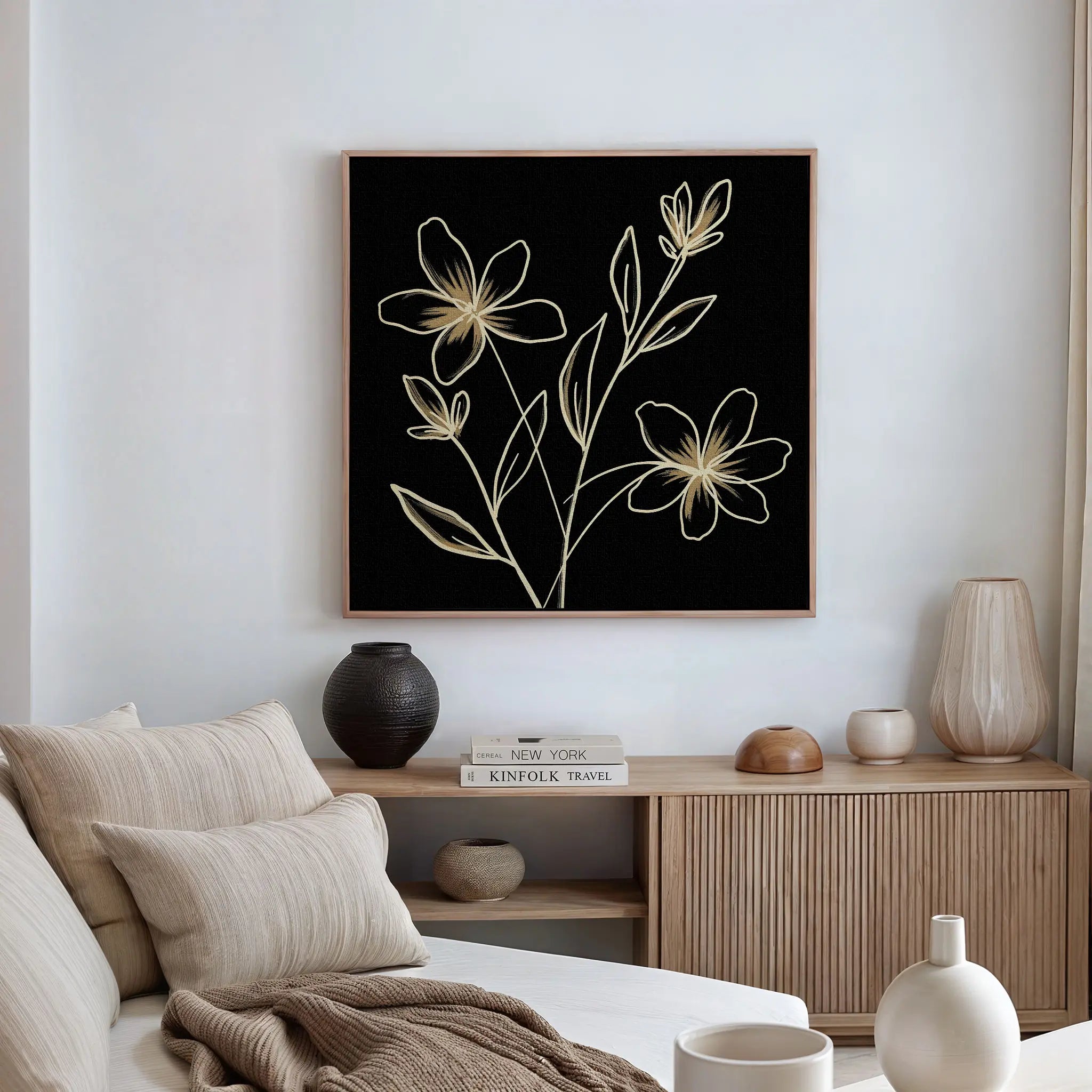 A modern living room with a beige couch, wooden sideboard, and decorative accents is highlighted by Golden Stems Canvas Art—striking floral wall art with minimalist gold line drawings on a black background.
