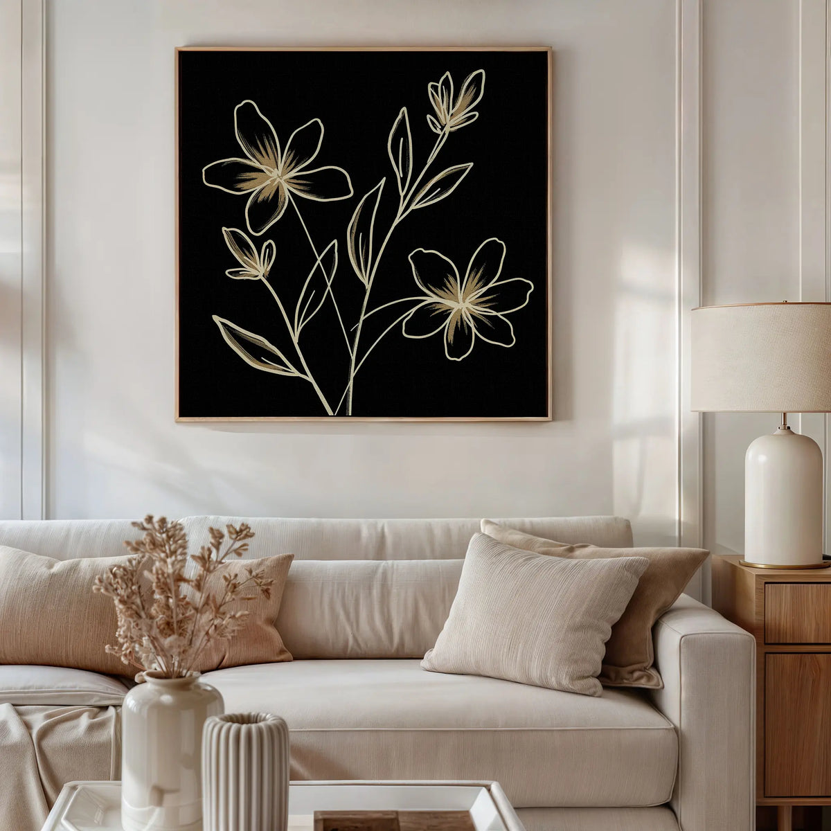 A neutral-toned living room with a white sofa, beige pillows, a wooden side table and lamp, dried flowers in a vase, and modern Golden Stems Canvas Art featuring minimalist floral line drawings on the wall.
