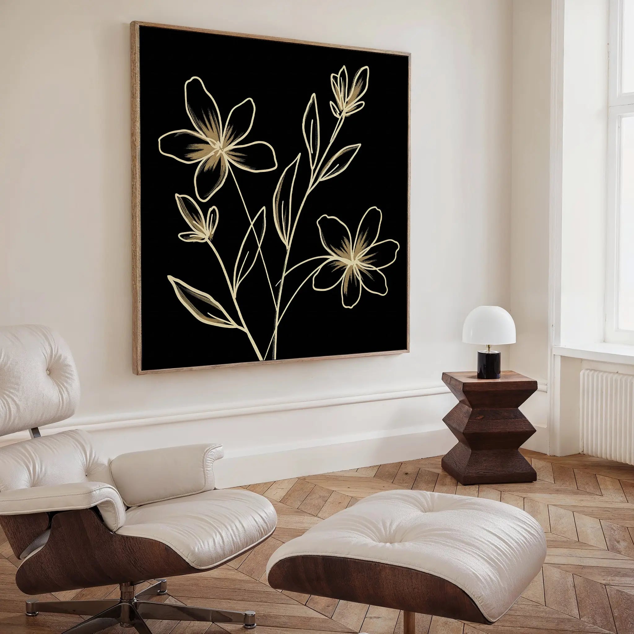 A modern living room with a white lounge chair and ottoman, dark wood side table with a white lamp, and the Golden Stems Canvas Art featuring gold floral line drawings. Light wood herringbone flooring completes the look.