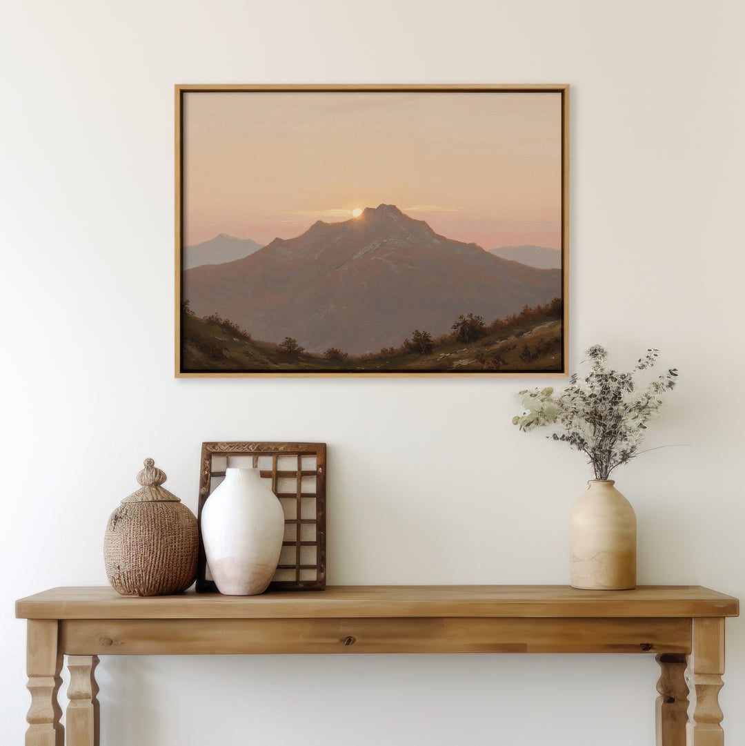A wooden table with neutral-toned vases and decor sits against a white wall, topped by the Golden Summit Canvas Art depicting a mountain sunset. Dried flowers and a woven basket complete this inviting living room scene.