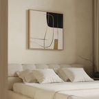 A modern bedroom with minimalist decor features a beige upholstered bed, white bedding, and Golden Thread Canvas Art in black, beige, white, and gold above the bed. A bare branch in a vase sits on the bedside table.