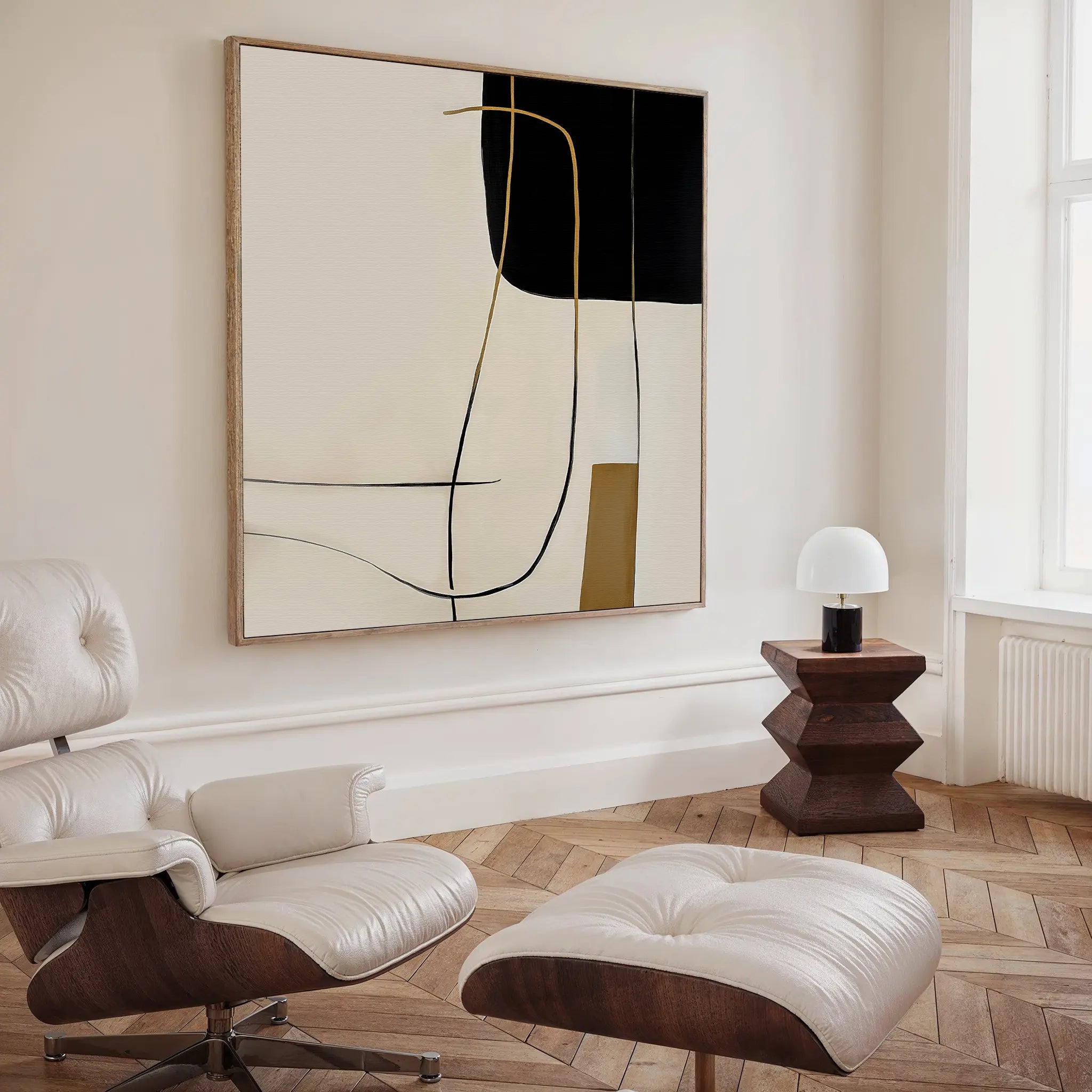 A modern, minimalist living room featuring a white leather lounge chair with ottoman, wooden side table and lamp, and the Golden Thread Canvas Art with bold black, white, and beige shapes—ideal for minimalist decor lovers.