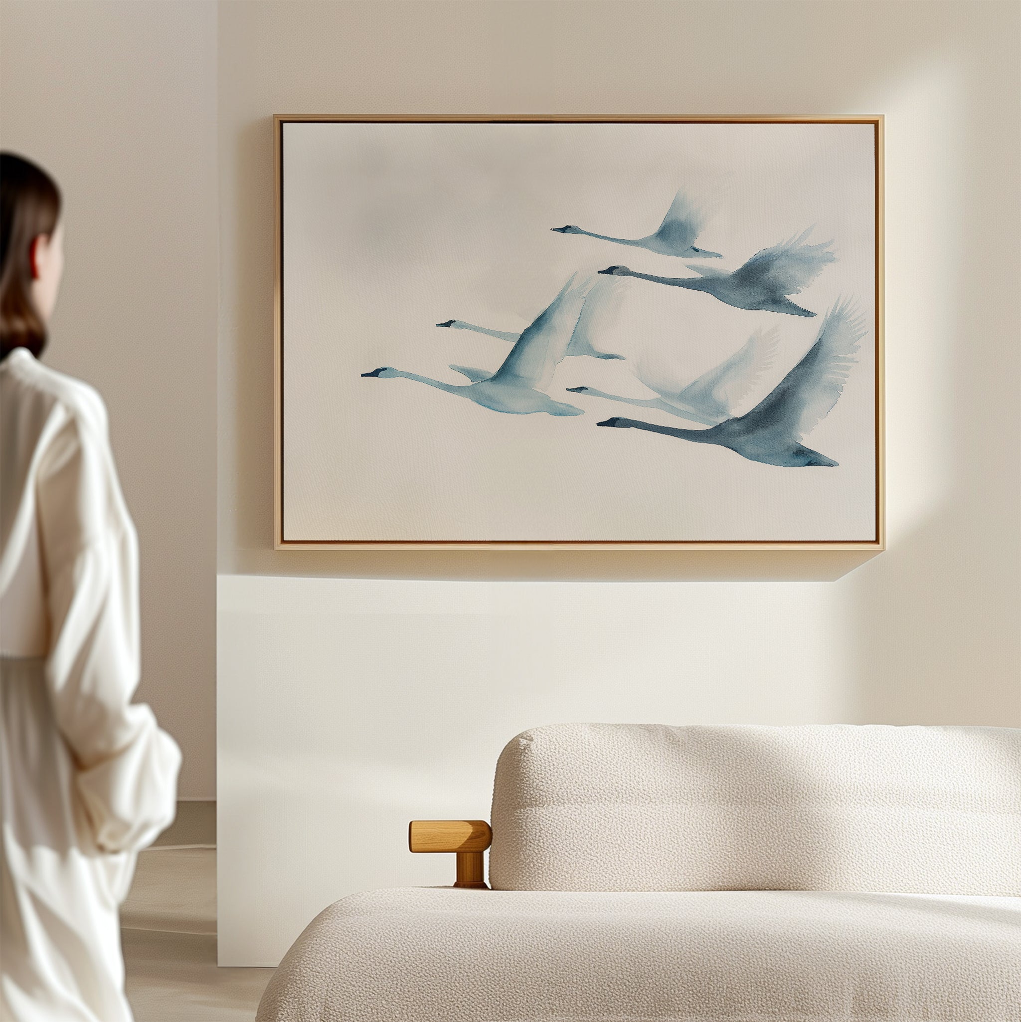 A woman stands in a bright, minimal room, admiring the Graceful Flock Canvas Art above a textured cream sofa—an elegant piece of modern nature decor.