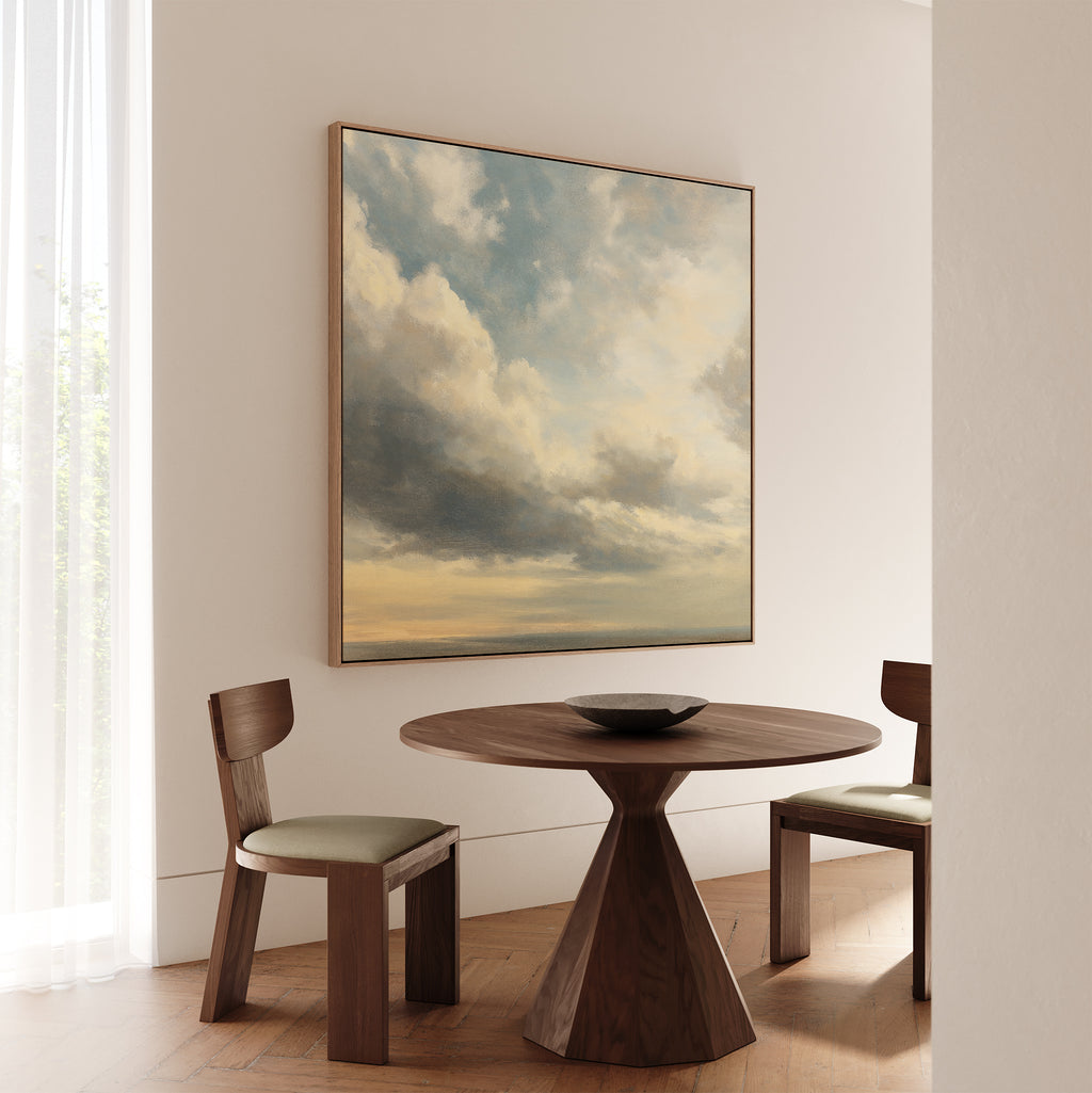 A minimalist dining area features two wooden chairs, a round table, and a black bowl. Sunlight streams through sheer white curtains, illuminating the serene space accented by the Heavenly Drift Canvas Art on the wall.