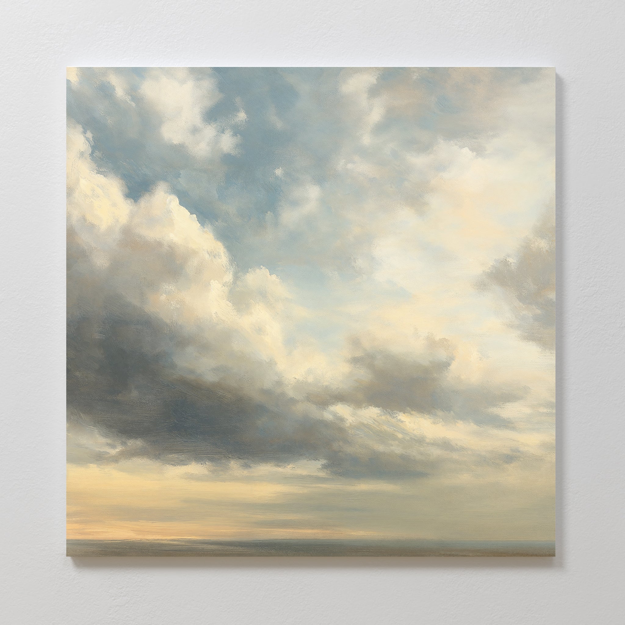 The Heavenly Drift Canvas Art features a square print of a cloudy sky with soft, sunlit clouds in blue, gray, and white above a hazy horizon. Ideal for vintage decor, its shown mounted on a white textured wall in a serene living room.