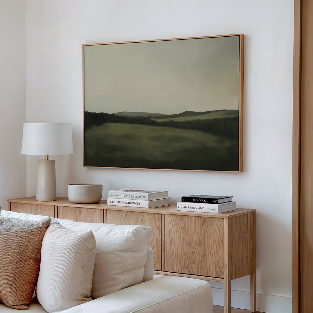 A light wood sideboard with books, a bowl, and a white lamp sits beneath the Hills at Dusk Canvas Art – Horizontal on a white wall in a neutral living room with a cream sofa.