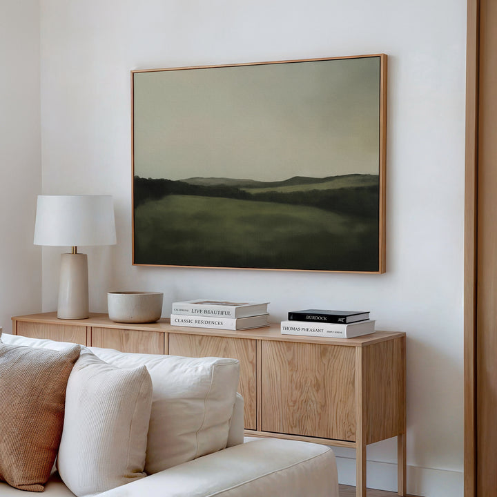 A light wood sideboard with books, a bowl, and a white lamp sits beneath the Hills at Dusk Canvas Art – Horizontal on a white wall in a neutral living room with a cream sofa.
