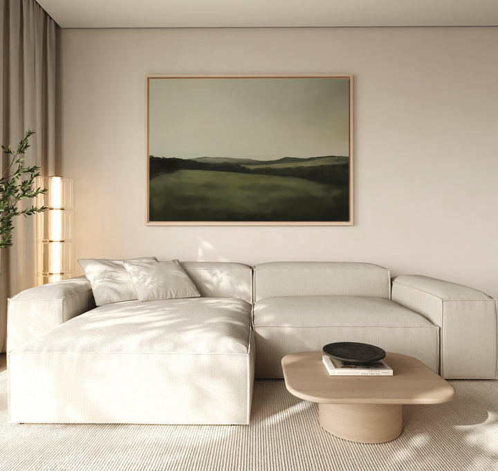 A modern living room with a light beige sectional sofa, a wooden coffee table, the Hills at Dusk Canvas Art – Horizontal on the wall, and a tall plant in the corner—all in neutral tones and bathed in natural light.