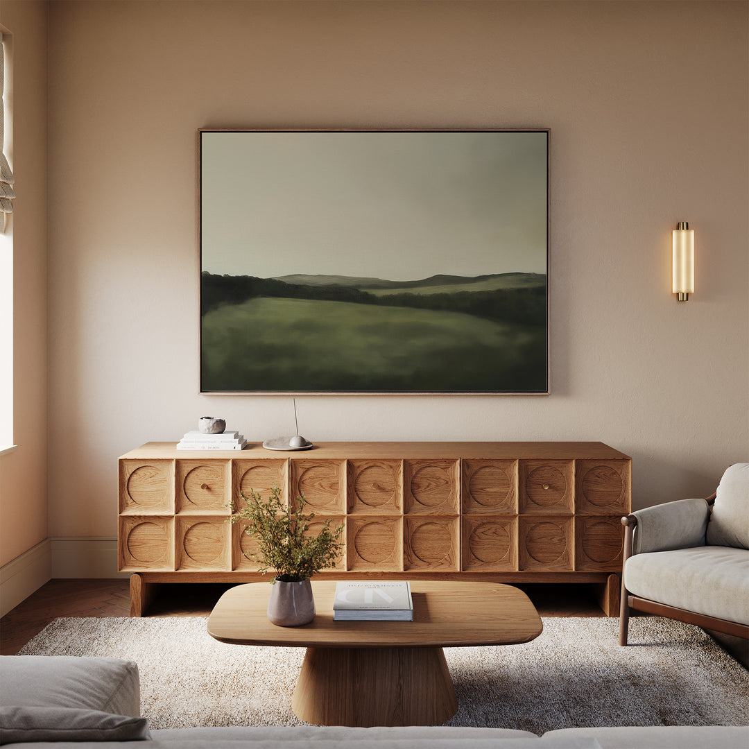 A minimalist living room with neutral tones features a wooden sideboard, soft rug, two light sofas, and the Hills at Dusk Canvas Art – Horizontal above the sideboard to add a stylish touch to the decor.