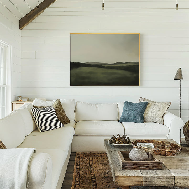 A cozy living room features a white sectional sofa, textured pillows, a rustic wooden coffee table, and neutral decor. Above the sofa, the Hills at Dusk Canvas Art – Horizontal hangs on a white shiplap wall, enhancing the inviting space.