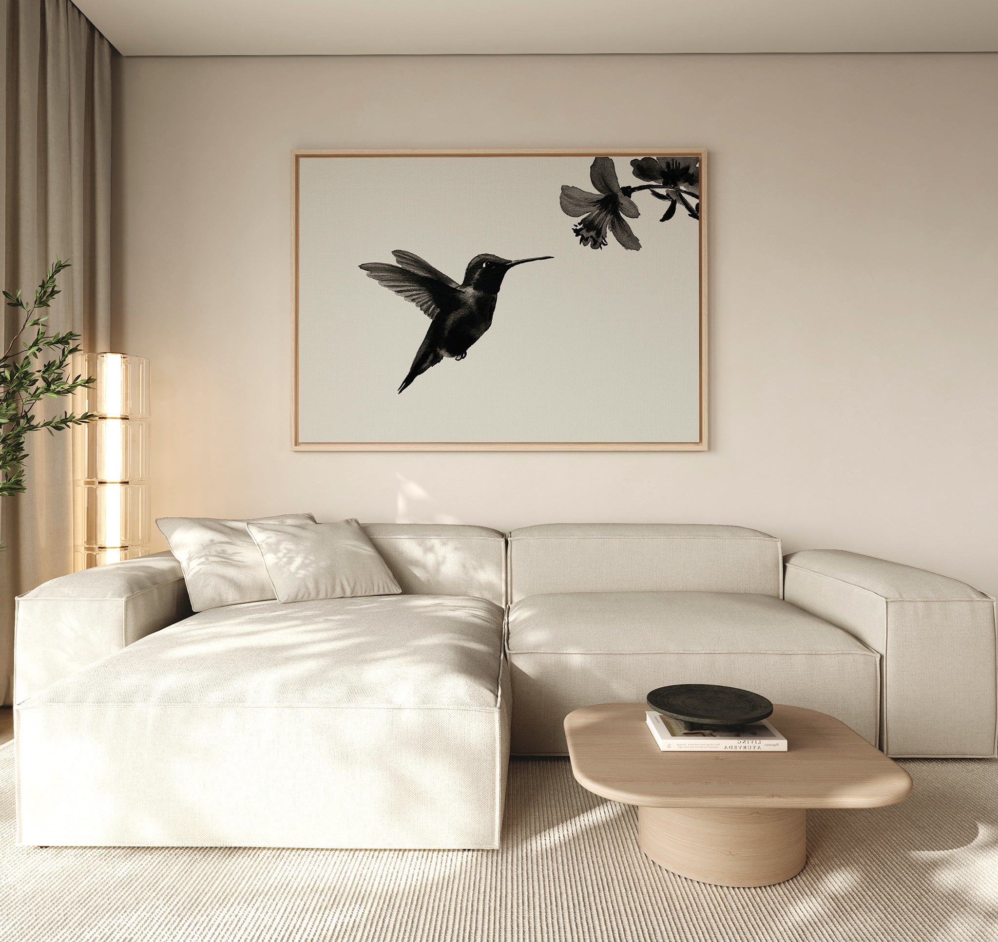 A modern living room features a light beige sectional sofa, a light wood coffee table, and the Hummingbird Motion Canvas Art—a large minimalist piece with a black hummingbird print—bathed in soft natural light that enhances the contemporary decor.