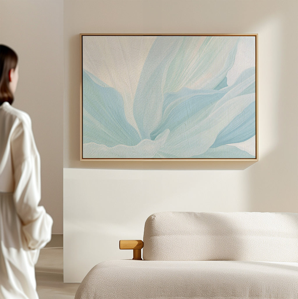 A person in a white shirt stands in a minimalist living room, admiring the Icy Petals Abstract Canvas Art in soft blue and beige tones above a light sofa—the perfect addition to elegant living room decor.
