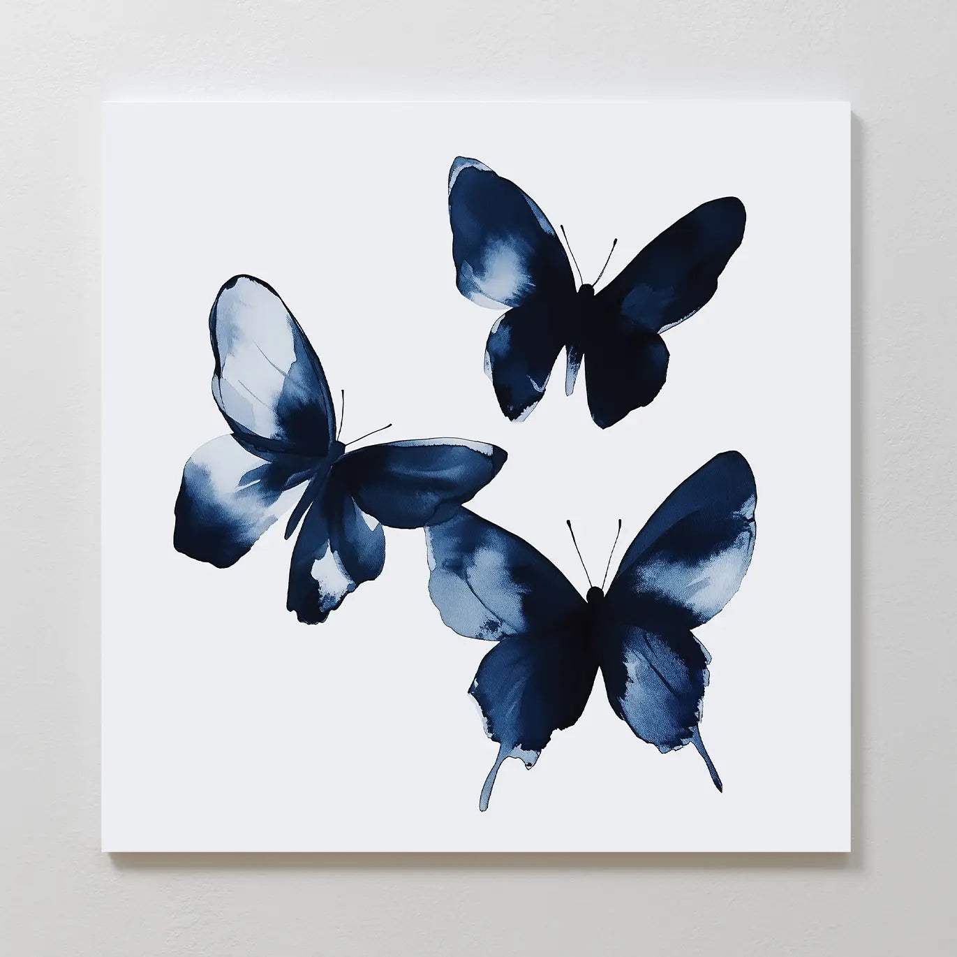 The Indigo Flutter Canvas Art showcases three abstract blue butterflies with unique wing patterns on a white background—a minimalist piece perfect for modern home decor.