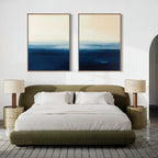 A modern bedroom with a low olive-green bed, white bedding, gold nightstands, a textured rug, and the Indigo Horizon Set of 2 wall art in blue and beige above the bed adds a calming touch to the stylish space.