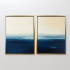 The Indigo Horizon Set of 2 features framed abstract art with deep blue to cream gradients, evoking a serene horizon. Perfect modern wall decor for your living room, displayed side by side on a white wall.