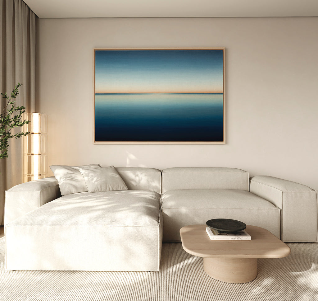 A modern living room features a light beige sectional, wooden coffee table, minimalist black bowl, and the Indigo Passage Canvas Art – Horizontal above the sofa, adding a stylish blue accent to the decor.