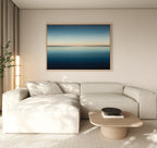 A modern living room features a light beige sectional, wooden coffee table, minimalist black bowl, and the Indigo Passage Canvas Art – Horizontal above the sofa, adding a stylish blue accent to the decor.