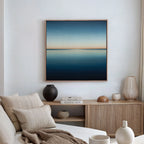 A minimalist living room with a beige sofa, textured cushions, a wooden sideboard with decorative objects, and modern decor featuring the Indigo Passage Canvas Art framed above the white wall.