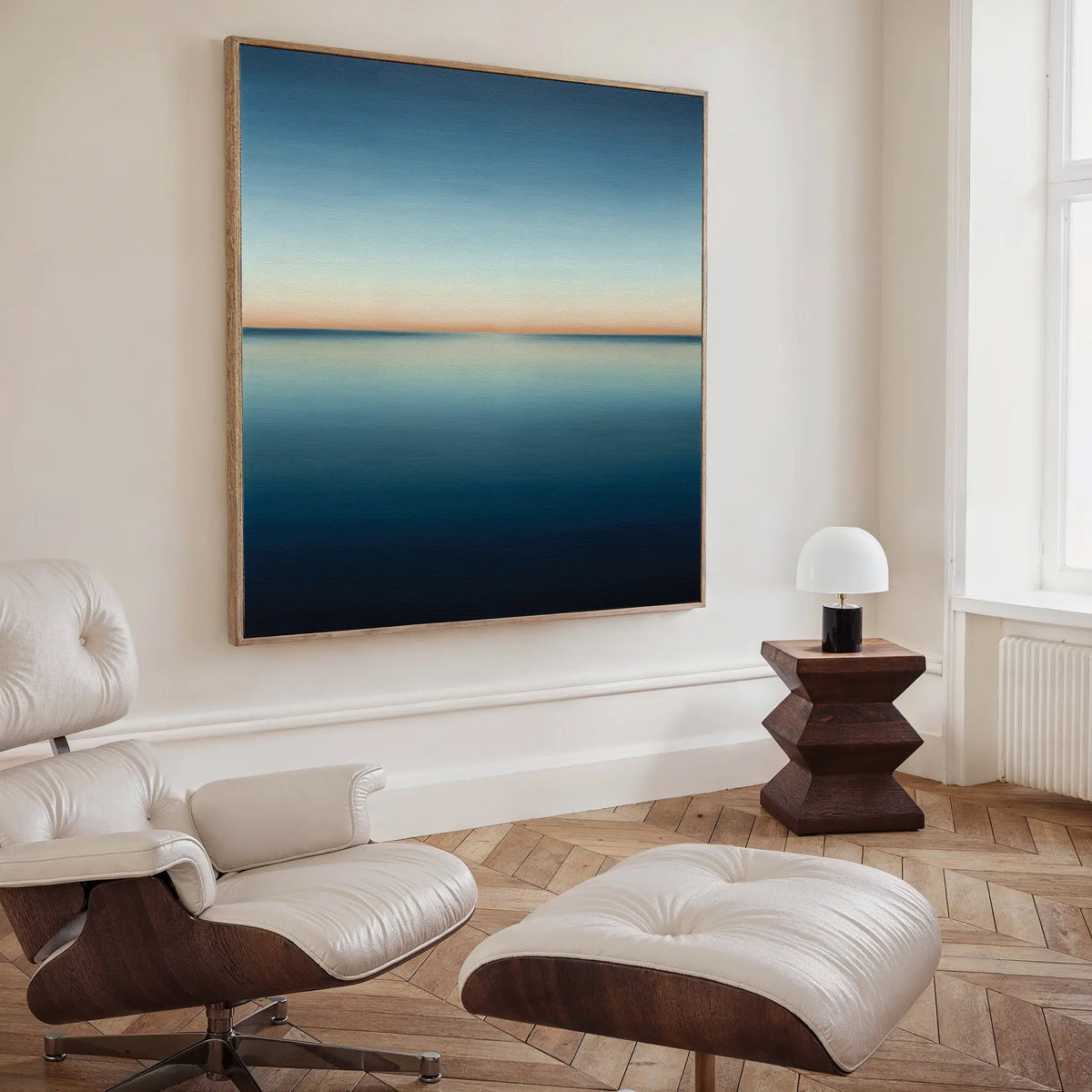 A modern living room with a white leather lounge chair and ottoman, a geometric wooden side table with a small lamp, and the Indigo Passage Canvas Art that enhances the modern decor.