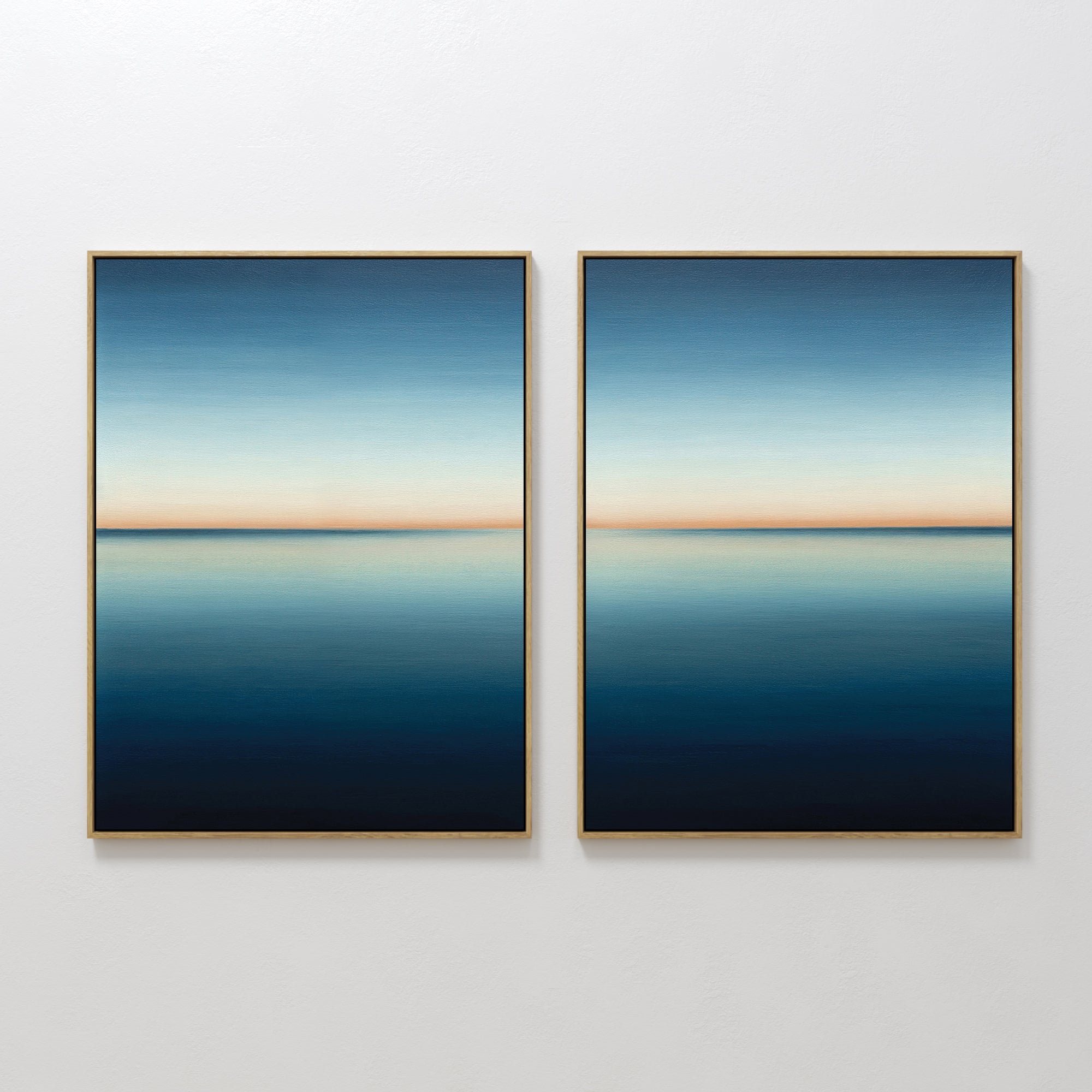 The Indigo Passage Set of 2 features minimalist wall art with framed paintings showing serene seascapes—calm blue water, a gentle horizon, and gradient skies fading from light to deep blue with a soft orange band.