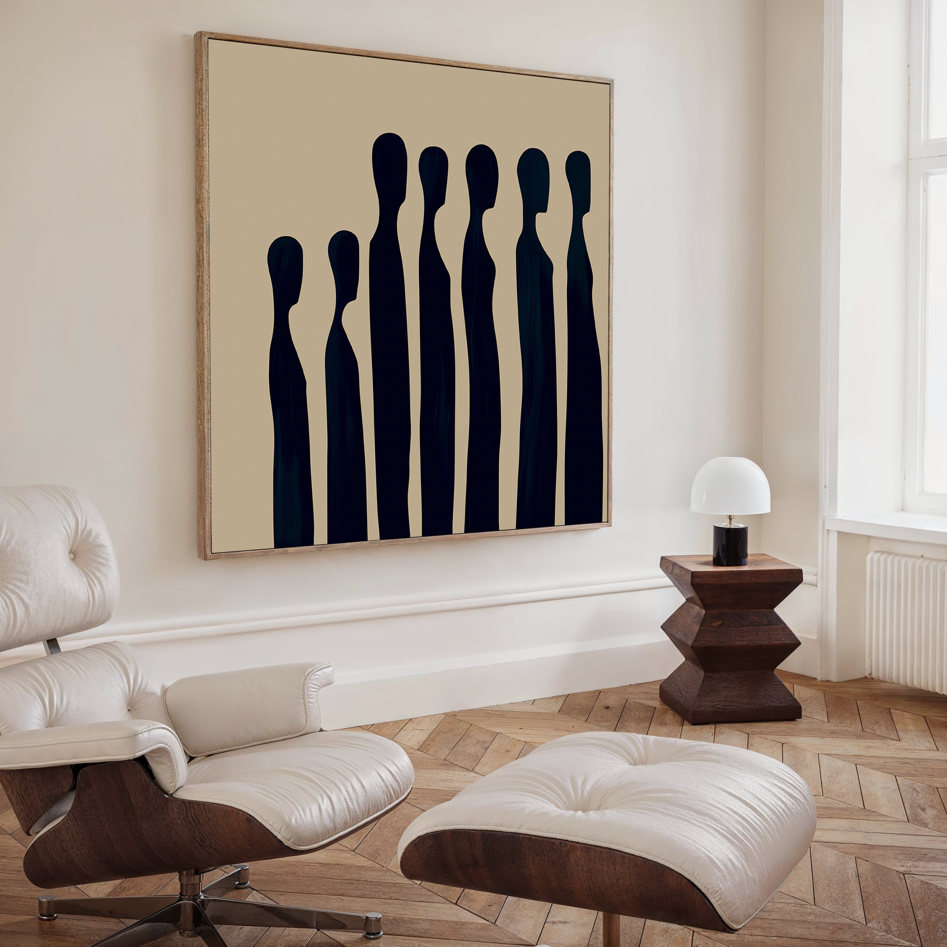 A modern living room featuring a white leather lounge chair with ottoman, wooden side table with white lamp, and Indigo Profile Abstract Canvas Art—tall, dark figures on beige—perfect for refined living room decor.