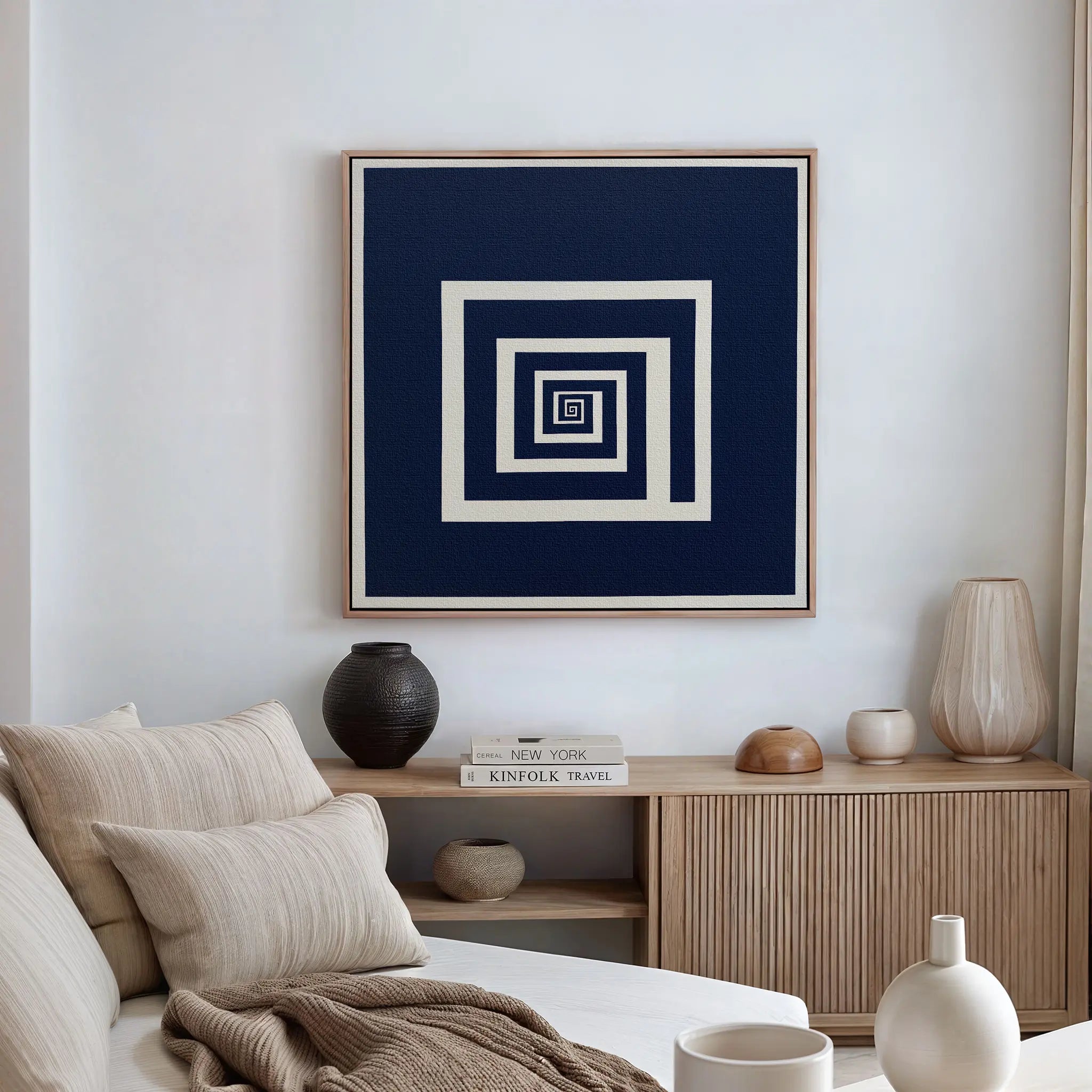 A modern living room features a neutral sofa with striped pillows, a wooden sideboard displaying modern decor, and the Infinite Descent Canvas Art—a minimalist wall piece with concentric navy and white squares—on the wall.