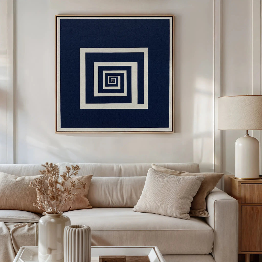 A modern living room with a beige sofa, neutral cushions, a table with dried flowers, and a lamp. Above the sofa, Infinite Descent Canvas Art featuring navy and white concentric squares adds a stylish modern touch.