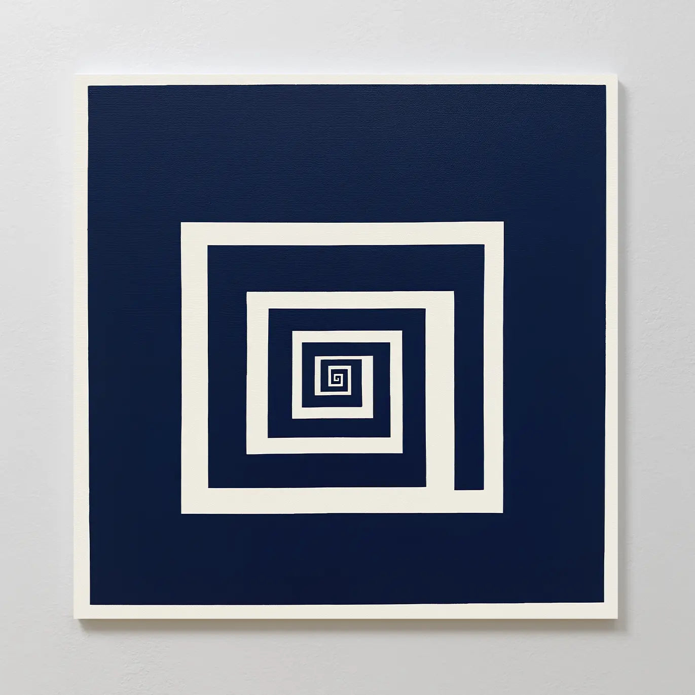 The Infinite Descent Canvas Art displays a navy blue background with a white geometric spiral of concentric squares, creating an optical illusion. This square, minimalist wall art is shown mounted on a light gray wall.