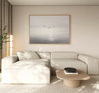 A modern living room with a beige sectional sofa, low wooden coffee table, light walls, and the "Into the Light Canvas Art – Horizontal" depicting birds over a calm sea above the sofa. A tall plant and sheer curtains are on the left.