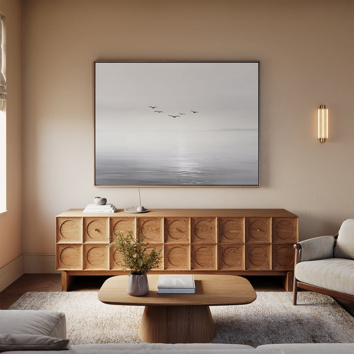 A modern living room features a wooden coffee table, geometric-patterned sideboard, light rug, white sofa, and the striking "Into the Light Canvas Art – Horizontal" above the sideboard—perfect for elegant decor.